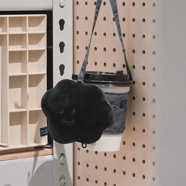 Black furry bag with a smiley face design hanging on a pegboard.
