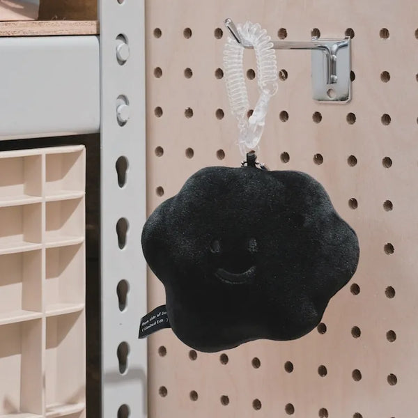 Black cloud-shaped plush toy with a smiley face hanging on a pegboard.