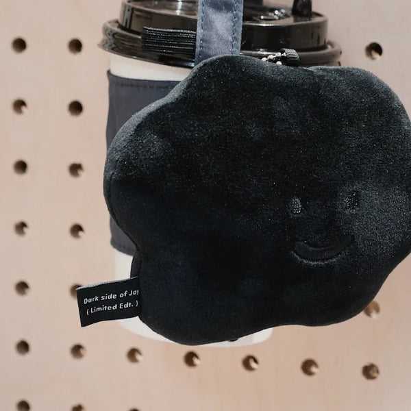 Black plush toy with a smiley face on a cup against a pegboard background