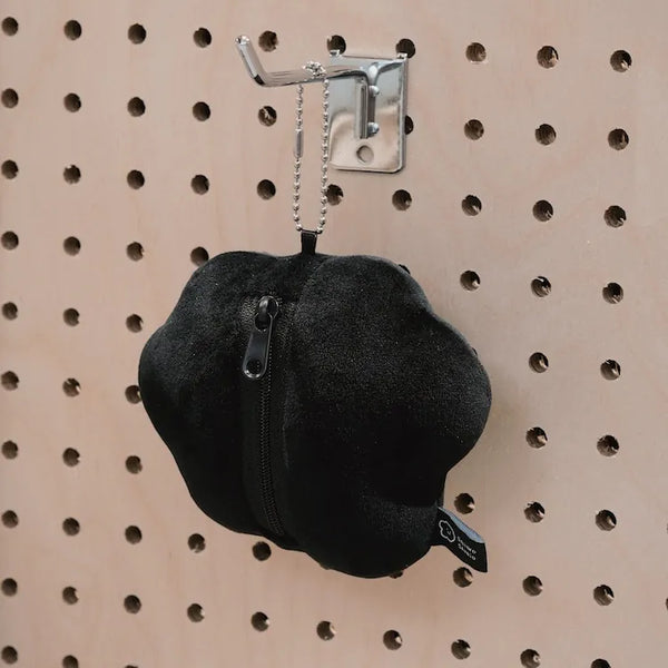 Black bean-shaped product with a zipper on a pegboard wall