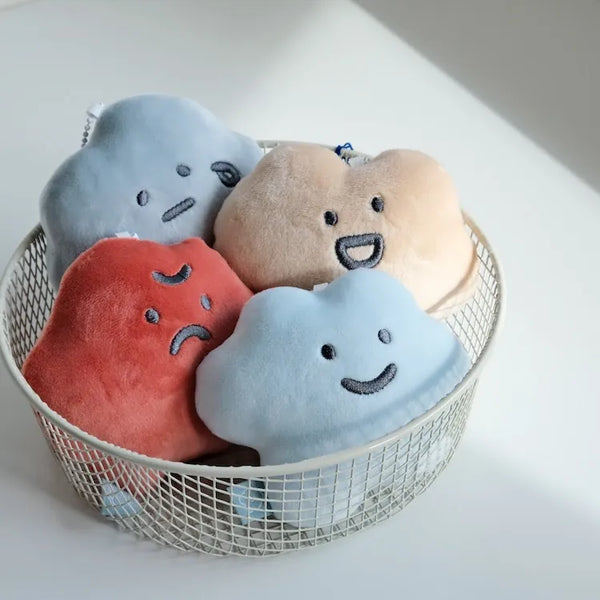 Set of plush cloud-shaped toys with facial expressions in a wire basket on a light background