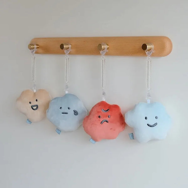 Four cloud-shaped toys with facial expressions hanging from a wooden rod against a white background.