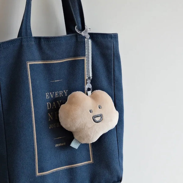 Plush cloud charm attached to a blue tote bag with text.