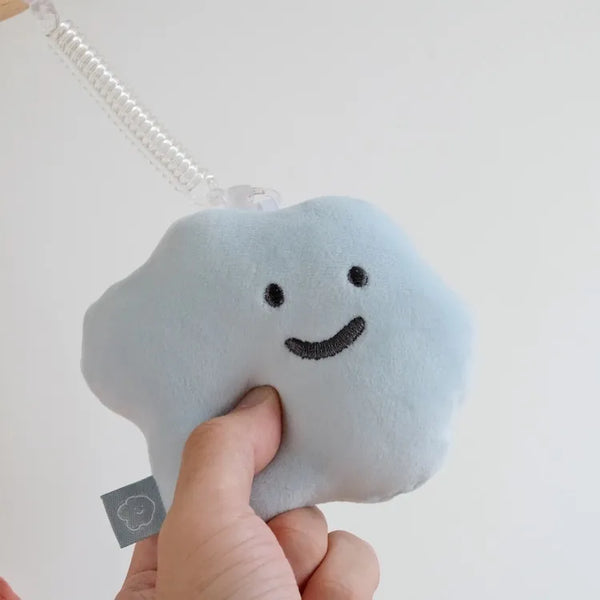Plush cloud-shaped toy with a smiley face held by a hand against a light background