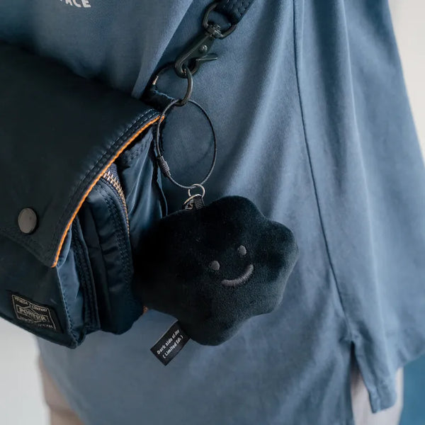 Black plush keychain with a smiley face attached to a blue jacket.