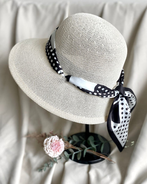 Beige straw hat with a black and white polka dot scarf on a neutral background