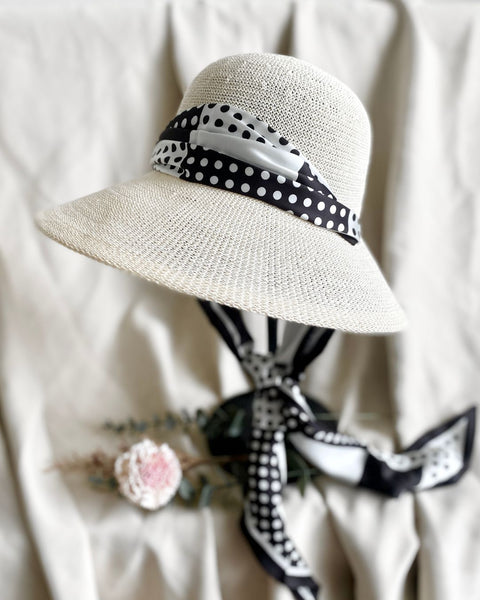 White straw hat with a black and white polka dot ribbon on a light background