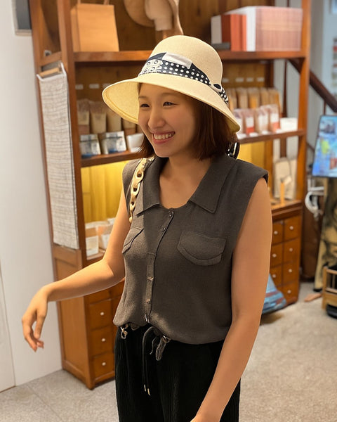 Woman wearing a beige hat with a black and white band, standing in a store.