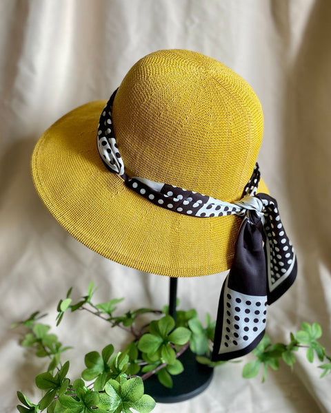Yellow sun hat with a black and white polka dot scarf on a mannequin head against a beige background.